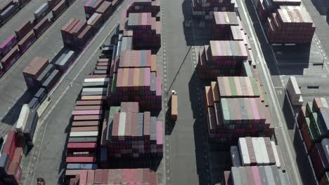 Aerial-view-following-truck-vehicle-moving-through-import-export-shipping-containers-distribution-storage-depot