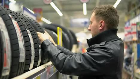 Young-man-looking-over-automobile-tyres-in-the-automotive-department-of-the-hypermarket-and-trying-to-choose