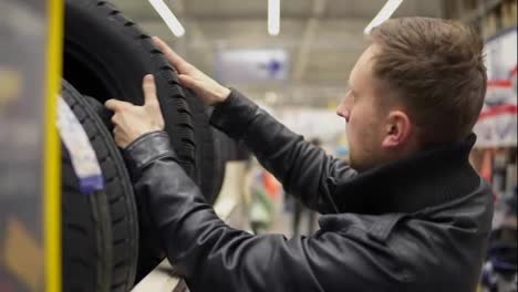 Young-man-looking-over-automobile-tyres-in-the-automotive-department-of-the-hypermarket-and-trying-to-choose-while-pressing-on-them