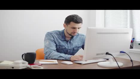 Young-businessman-working-on-computer-in-stylish-modern-office.-Computer,-phone-and-cup-on-the-table.-Shot-in-4k