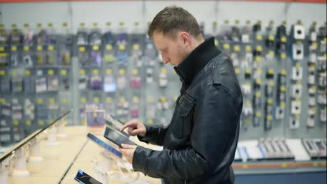 Young-male-customer-choosing-a-new-tablet-in-a-shop,-checking-how-it-works
