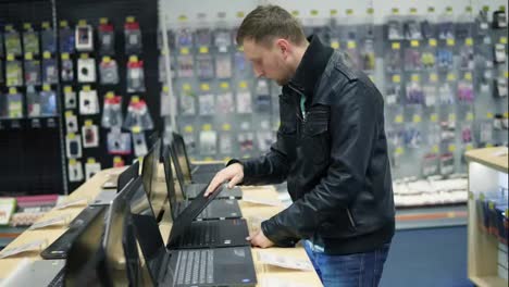 Young-man-in-the-electronics-supermarket-is-choosing-a-laptop.-Variety-of-laptops-on-the-shelves