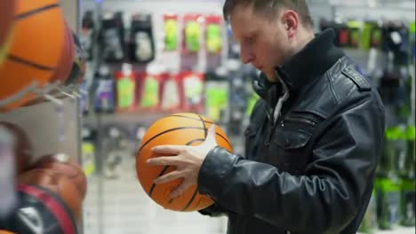 An-adult-man-in-black-leather-jacket-examines-the-balls-that-lie-on-the-shelves-in-the-supermarket.-A-man-looks-at-a-basketball-ball-for-outdoor-sports
