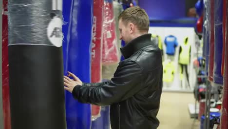 An-adult-man-in-black-leather-jacket-choosing-a-punching-bag-in-a-sports-store