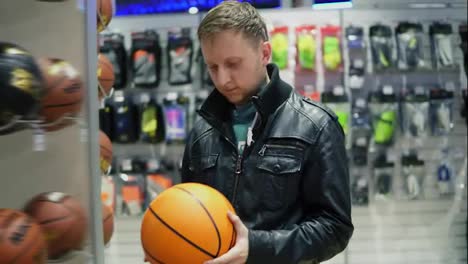 An-adult-man-in-black-leather-jacket-choosing-a-basketball-ball-in-a-sports-store
