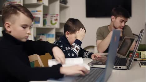 Dos-Niños-Pequeños-Escribiendo-Algo-En-Los-Teclados-De-Una-Computadora-Portátil-Mientras-Su-Maestro-Programador-Está-Sentado-Cerca.