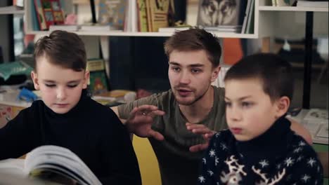 Slow-motion-footage-of-young-attractive-male-teacher-explaining-something-to-his-two-little-pupils-boys-on-a-programming-class.-Educational-process.