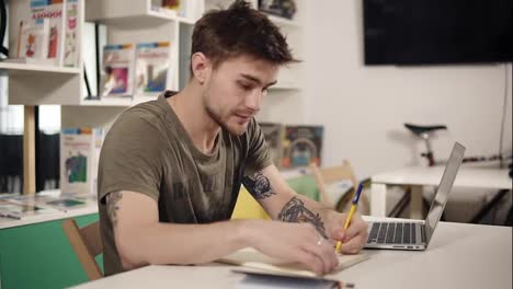 Attractive-young-male-programmer-teacher-writes-something-down-in-his-notebook,-looking-very-serious.