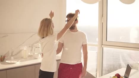 Attractive-young-caucasian-couple-meet-early-morning-in-the-home-modern-kitchen.-Wearing-domestic-clothes,-embracing,-husband-kissing-his-wife-.-Happy-married-couple-enjoying-morning