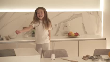 Happy-beautiful-little-girl-dancing-in-modern-kitchen-having-fun-doing-funny-dance-moves.-Long-haired,-smiling-girl-enjoying-weekend-at-home.-Slow-motion