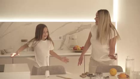 Happy-family-in-the-modern,-white-kitchen.-Mom-and-daughter-in-white-casual-clothes-relaxfully-dance.-Mom-is-dancing-with-her-daughter-in-the-kitchen.-Slow-motion