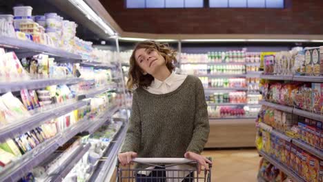 Portrait-of-happy,-relaxful-woman-with-curly-hair-went-shopping-with-trolley-cart---walk-by-a-row-and-happily-dancing-in-relaxful-mood.-Slow-motion