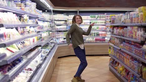 Full-length-footage-of-young-woman-in-jeans-and-sweater-dancing-standing-at-grocery-store-aisle-with-big-assortment.-Excited-woman-having-fun,-dancing-supermarket.-Slow-motion