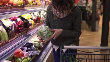 Young-woman-in-modern-supermarket-choosing-big-cabbage-in-organic-vegetable-department-and-put-it-to-a-cart.-Healthy-female-buying-green-food.-Concept-fresh,-assortment,-vegetarian-girl-in-grocery-store