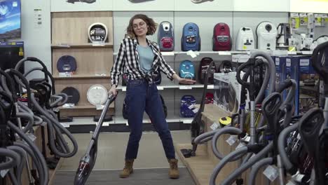 Funny-caucasian-woman-in-casual-standing-in-home-appliance-store---dancing,-having-fun-with-hand-helded-vacuum-cleaner,-funky-dances