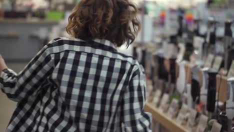 Rare-view-of-cute-caucasian-pretty-young-woman-with-short-curly-hair-and-in-headphones-dancing-and-listening-music-in-the-middle-of-the-supermarket-with-household-stuff