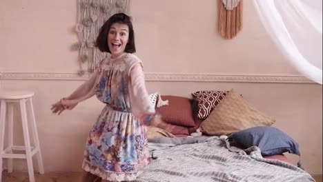 Cheerful-happy-young-brunette-girl-with-short-hair,-wearing-beautiful-dress,-jumping-or-falling-on-comfy-bed.-Indoors-footage