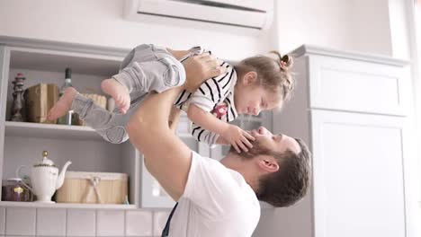 Dad-holds-a-small-daughter-in-his-arms-in-the-kitchen,-daughter-kisses-her-father-on-the-kitchen