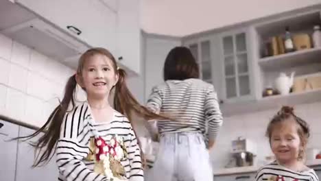 Two-daughters-are-dancing-on-the-kitchen,-mother-are-cooking-behind-them