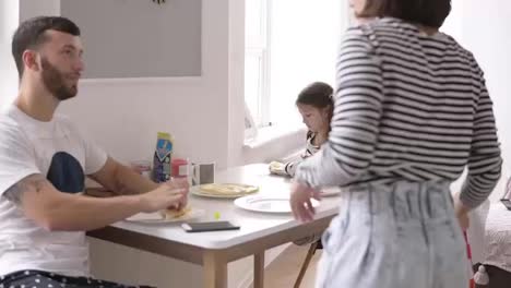 Young-family-at-home-kitchen-eating-breakfast-together-with-two-daughters-and-talking