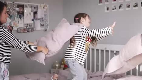 Funny-family-having-a-pillow-fight-in-bed.-Mother-kicks-her-daughter-with-pillow-and-she-falling-down.-Making-fun.-Slow-motion