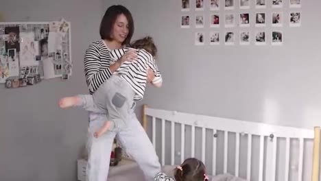 Modern-mother-of-two-is-playing-with-her-little-daughter-swinging-her-and-tickling-in-slow-motion-while-her-older-daughter-laughing-and-playing