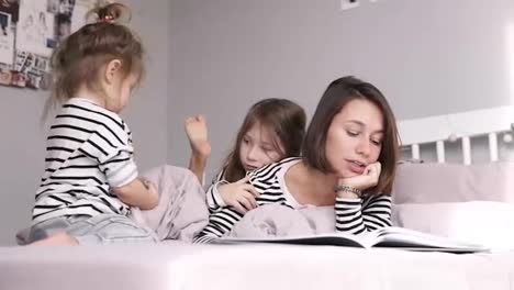 Mother-is-reading-a-book-for-her-two-daughters-lying-on-a-bed.-Identical-clothes