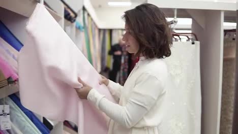 A-beautiful-brunette-chooses-a-fabric-in-a-tissue-store.-Takes-a-roll-of-light-pink-fabric-and-applies-to-the-body.-Tries-on.-Slow-motion