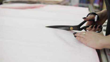 Extremely-close-up-footage-of-a-female-seller-cutting-the-light-colored-tissue-using-a-black-scissors.-Fabric-is-on-the-table