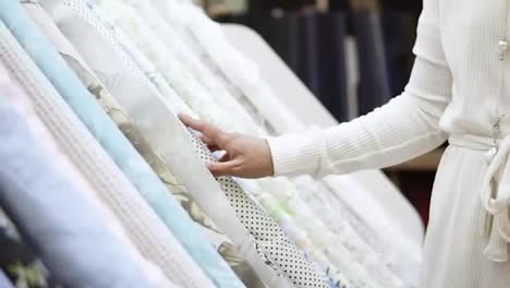 A-beautiful-girl-shopper-in-a-fabric-store.-She-chooses-a-roll-of-fabric-with-polka-dots-among-the-range-of-light-fabrics.-Slow-motion