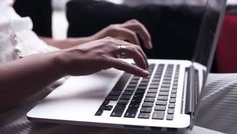Aim-footage-of-a-young-women's-hands-typing-on-a-silver-laptop.-Computer-is-on-her-legs.-Black-screen