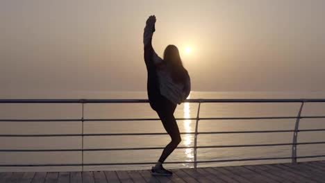Girl-showing-incredible-flexibility-of-the-body.-She-stretches-her-legs-while-standing-on-the-promenade-near-the-sea.-Morning-sun.-Bends-into-an-arch-standing-in-a-vertical-twine