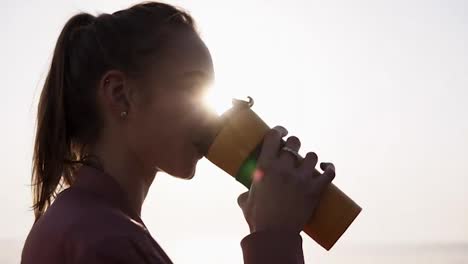Close-up-of-a-beautiful,-dreaming-young-woman.-Girl-is-enjoying-the-moment.-Drinks-from-a-sports-mug.-Breathing.-Sun-is-shining-on-the-background