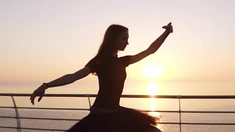Beautiful-scene-of-a-dancing-ballerina-in-tutu-and-pointe-near-ocean-or-sea-at-sunrise-or-sunset.-Young-sensual-woman-with-long-hair-practicing-classic-exercises.Slow-motion
