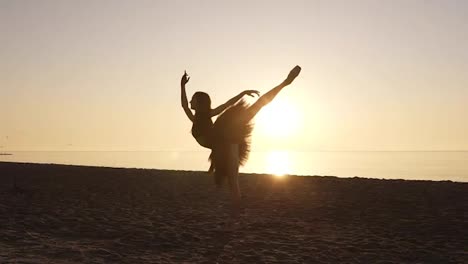 Silhouette-of-a-ballerina-in-a-tutu-and-pointe-shoes-on-the-seashore.-Practicing-in-ballet-movements-and-poses.-Morning-sunrays-around-the-elegant-ballet-dancer-body.-Slow-motion