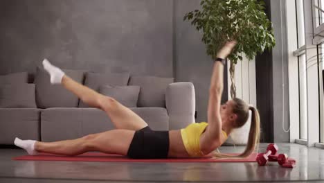 Aerobics-sport-exercises,-female-sporty-is-raising-the-legs-up-trying-touch-it-with-hands-while-laying-on-the-exercise-red-mat.-Wearing-yellow-top-and-shorts.-Domestic-workouts