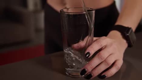 Close-up-woman-hands-with-dark-manicure-pours-the-water-into-glass-standing-on-kitchen-table.-Healthy-eating,-water-after-workout