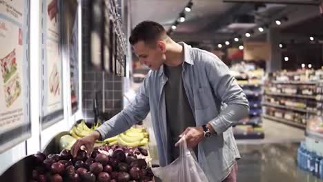 Side-footage-of-a-caucasian-man-chooses-red-onions-in-a-supermarket.-The-positive-tall-guy-in-blue-shirt-buys-food-and-vegetables-at-the-grocery-store.-Slow-motion