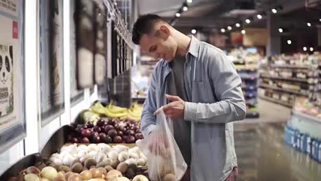 Handsome-caucasian-man-put-potatoes-in-the-transparent-plastic-packing-bag.-Shopping---man-chooses-nice-potatoes-adds-to-the-package.-Big-bright-grocery-store