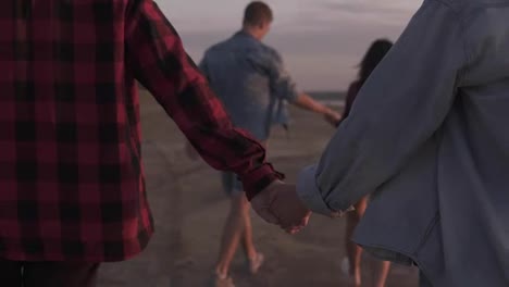 Happy-man-and-woman-couple-walking-and-holding-hands-on-a-deserted-beach-with-evening-dusk-sky.-Two-couple-walking-outdoors.-Youth-culture.-Happy-young-people