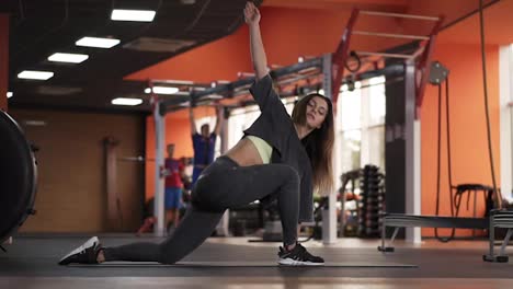 Flexible-european-woman-practice-yoga-postures-and-doing-stretching-in-gym-with-sports-equipment-on-background.-Slim-girl-doing-breathing-exercise-and-stretch-body-on-mat.-Female-pilates-body-care-concept.-Side-view