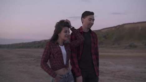 Beautiful-young-couple-in-plaid-shirts-are-walking-outdoors-on-a-sandy-teritory-in-the-evening.-Caucasian-brunette-couple,-friendship,-hanging-out-together