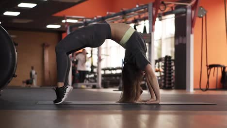 Young-lady-is-doing-upforward-bow-pose-in-modern-gym,-slow-motion.-Sportive-woman-is-demonstrated-bridge-position-and-stand-on-tiptoe-to-stretch-body