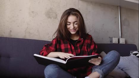 Young-attractive-brunette-girl-saying-something-and-smiling-while-reading-a-book.