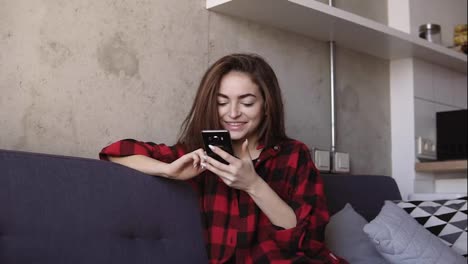 Attractive-young-brunette-girl-smiling-and-scrolling-the-smartphone.