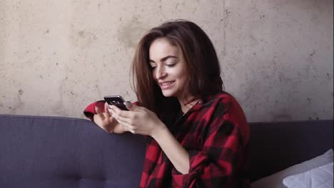 Young-beautiful-brunette-girl-looks-at-her-smartphone-and-acts-surprised.