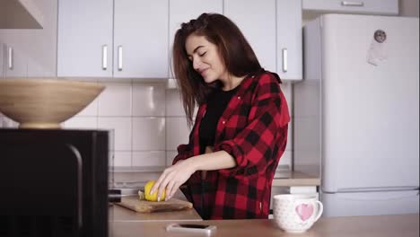 Young-beautiful-girl-in-red-flannel-shirt-slicing-lemon-and-then-making-herself-a-cup-of-tea-in-the-kitchen.