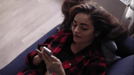 Young-brunette-girl-texting-to-someone-while-lying-on-sofa.