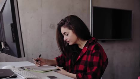 Young-attractive-girl-in-red-flannel-shirt-writing-something-down-in-her-notebook,