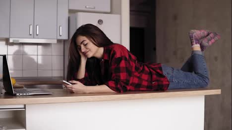 Beautiful-girl-in-her-20's-lying-on-her-kitchen-table-surface-an-texting-someone.